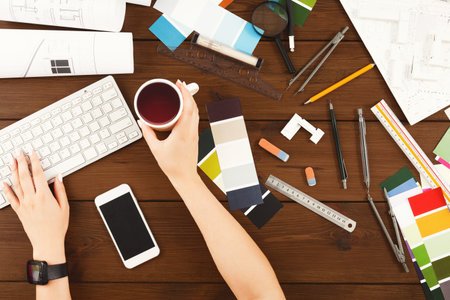 Creative Workspace Offers a View of Design Tools While a Hand Holds a Cup of Drink