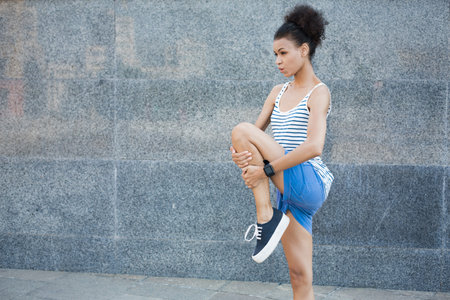 Young Woman Stretching Leg in Urban Setting During Daytime Near Gray Wall
