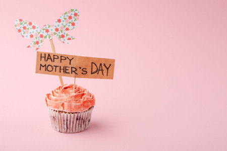 Cupcake With a Happy Mothers Day Sign and Butterfly Decoration on a Pink Background