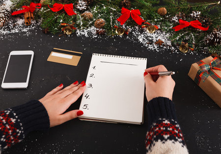Creating a Holiday Gift List With a Notebook and Pen on a Decorated Table