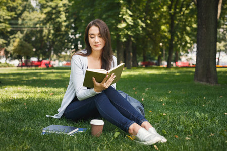 Woman Sitting on Grass Reading Book in a Park During the Day