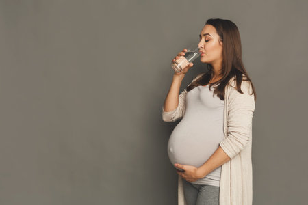 Pregnant Woman Enjoying a Glass of Water in a Simple Setting During Daytime Hours