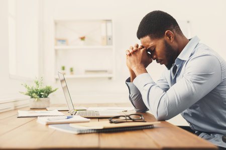 Young Man Focused on Work While Sitting at Desk With Laptop and Notes During Daylight Hours