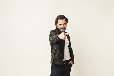 Man Points at Camera While Wearing a Leather Jacket in a Neutral Setting During Daylight