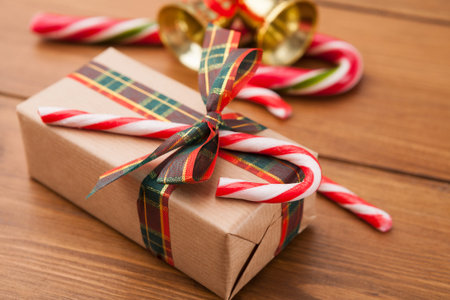 Christmas Gift Wrapped in Paper With Candy Canes and Bells on a Wooden Table