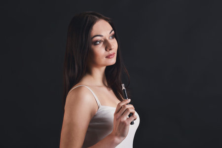 Woman Holds Vape Device in Studio Setting With Dark Background During Indoor Sessionの写真素材
