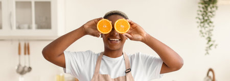Person Holds Orange Slices in Front of Face and Smiles in Bright Kitchenの写真素材