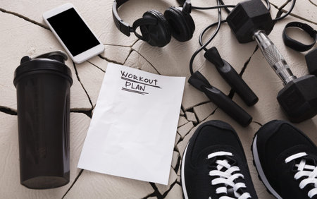 Workout Plan and Equipment Located on a Cracked Surface With a Smartphone and Headphones Nearby