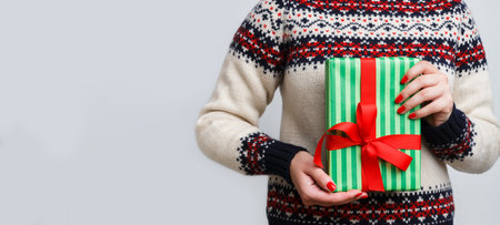 Gift Wrapped in Green and Red Held by Person Wearing Festive Sweater for Holiday Seasonの写真素材