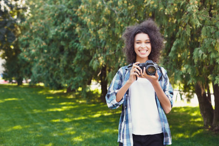 Person Stands in a Green Park Holding a Camera While Smiling With Trees Behindの写真素材