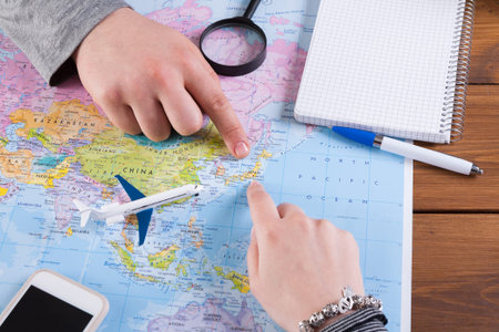 Planning a Trip Using a Map With Hands Pointing at Locations and Travel Tools on a Table