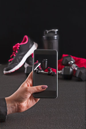 Person Taking a Picture of Workout Gear on a Black Background With a Smartphone