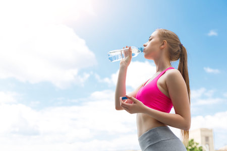 Woman Drinks Water During Outdoor Workout Under Blue Sky in Bright Daylight