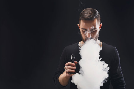 Man Vapes and Exhales Vapor While Standing in a Dark Space During an Indoor Activity