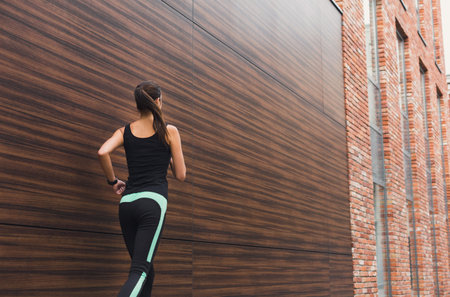 Woman Runs in Active Wear Against Wooden and Brick Wall Background in Urban Setting