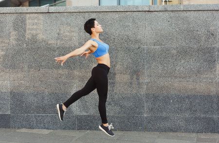 Dancer Performs a Jump in a Sunny Urban Space Near a Stone Wall