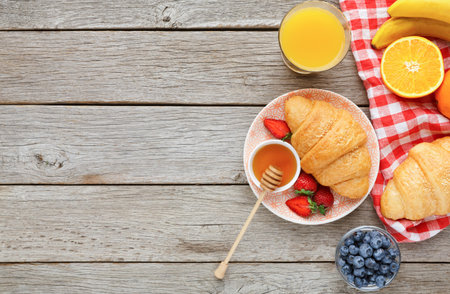 Display of Breakfast Items Featuring Croissants, Fruits, and Drinks on Wooden Tableの写真素材