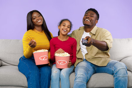 Family Enjoys Popcorn and Movie Night at Home While Sitting on a Sofa Together