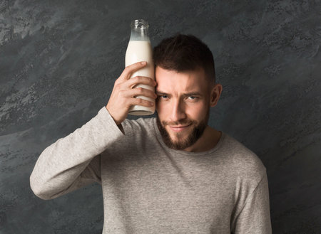 Man Holds a Glass Milk Bottle to His Head While Posing Against a Textured Background