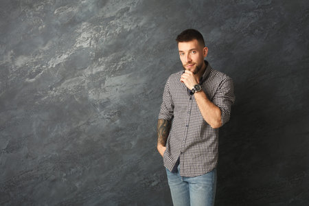 A Man Stands Against a Grey Wall, Displaying a Thoughtful Expression