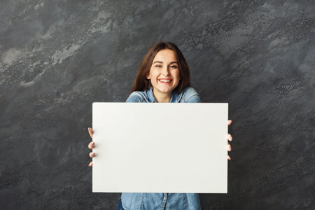 Woman Holds Blank Canvas for Artwork Display in Studio Setting With Gray Background and Bright Smile