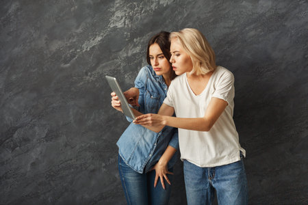 Two Women Viewing a Tablet Together in a Modern Indoor Setting With a Gray Background