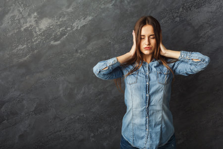 Woman Covers Ears in Front of Gray Wall in Urban Setting During Quiet Moment of Reflection