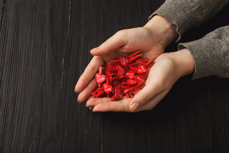 Hands Holding a Collection of Small Red Hearts on a Black Wooden Surface