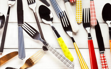 Set of Colorful Cutlery Arranged on a White Wooden Surface in a Flat Lay Design