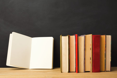 Collection of Books and a Blank Notebook on a Wooden Table Against a Dark Backgroundの写真素材