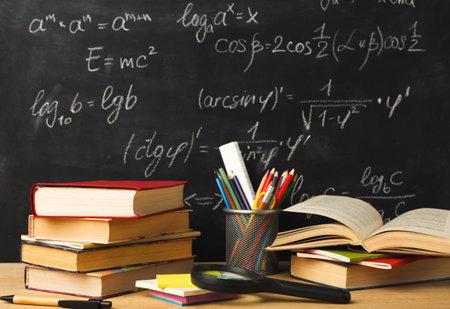 Collection of Books and Study Tools on Desk With Chalkboard in Backgroundの写真素材