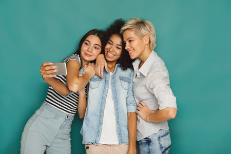 Three Friends Take a Selfie Together in Front of a Blue Background During a Fun Moment