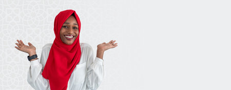 Woman in Red Hijab Smiling and Showing Hands With Open Palms in a Bright Settingの写真素材