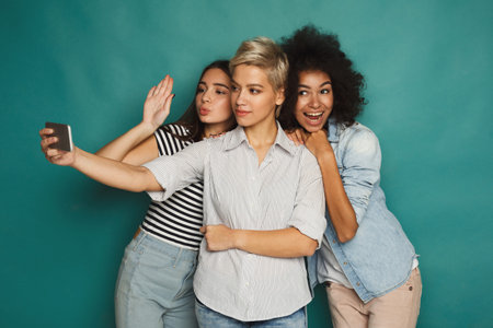 Three Friends Take Selfies Together in a Studio With a Blue Background During a Fun Gathering
