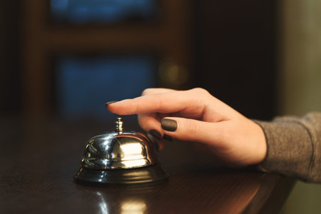 Hand Pressing Bell at Front Desk in a Lobby During Early Evening Hours