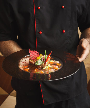 Chef Presents a Carefully Arranged Dish on a Black Plate in a Restaurant Setting
