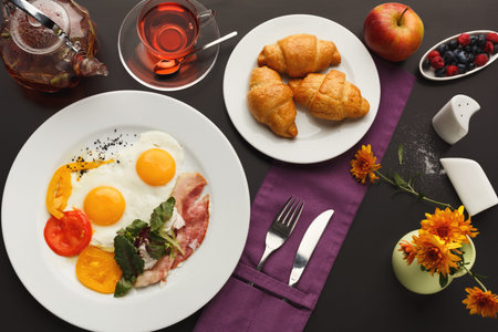 Breakfast Collection With Eggs, Croissants, Fruit, and Tea on a Dark Table