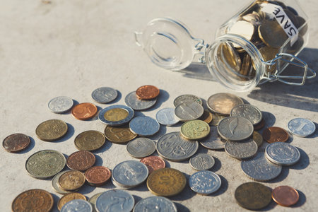 Collection of Coins Scattered Around a Glass Jar Labeled With the Word Save