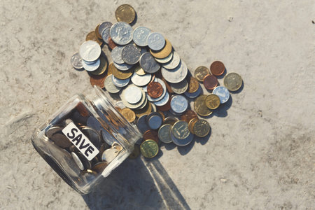 Saving Coins in a Jar Next to a Pile of Scattered Coins on a Flat Surface