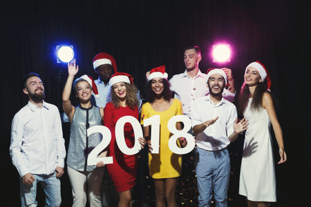 Collection of Friends Celebrating New Years Eve With Santa Hats and a Large Sign for 2018