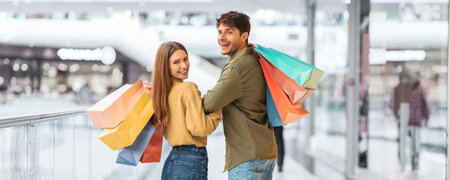 Young Couple Enjoying Shopping Together in a Busy Mall With Colorful Bagsの写真素材