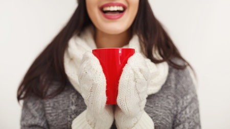 Woman wearing winter clothes drinking tea at white background