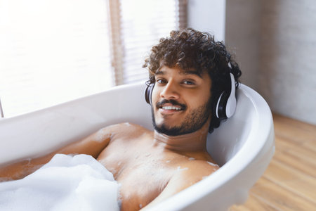 Man Relaxes in Bathtub With Headphones Enjoying Music on a Sunny Day at Homeの写真素材