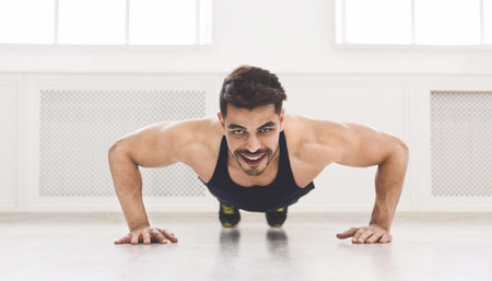 Young muscular man pushing ups in studio