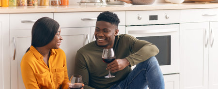 Cheerful Black Couple Sitting On Floor In Kitchen And Drinking Wine