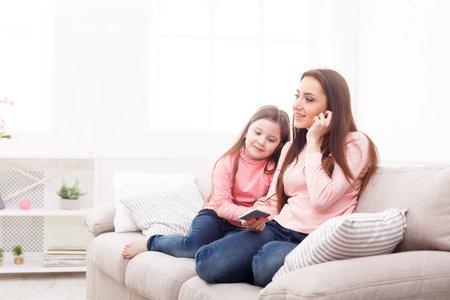 Mother and Daughter Enjoy Time Together on a Sofa With a Smartphone in a Bright Roomの写真素材