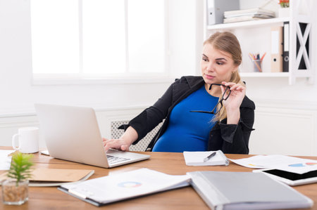 Woman Working at Home on Laptop While Pregnant During Daytime Hoursの写真素材