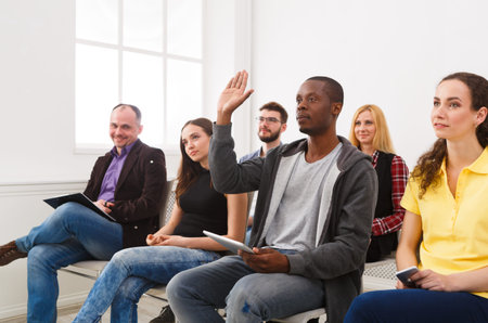 Group of People Sitting in a Room With One Person Raising Hand to Ask a Question During a Meeting