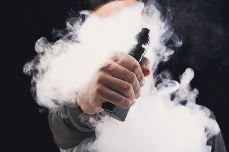 Person Holding Vape Device While Exhaling Vapor in Indoor Setting During Evening Time