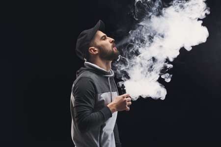 Man Exhales Vapor While Holding a Vape Device in a Dark Room During Nighttime